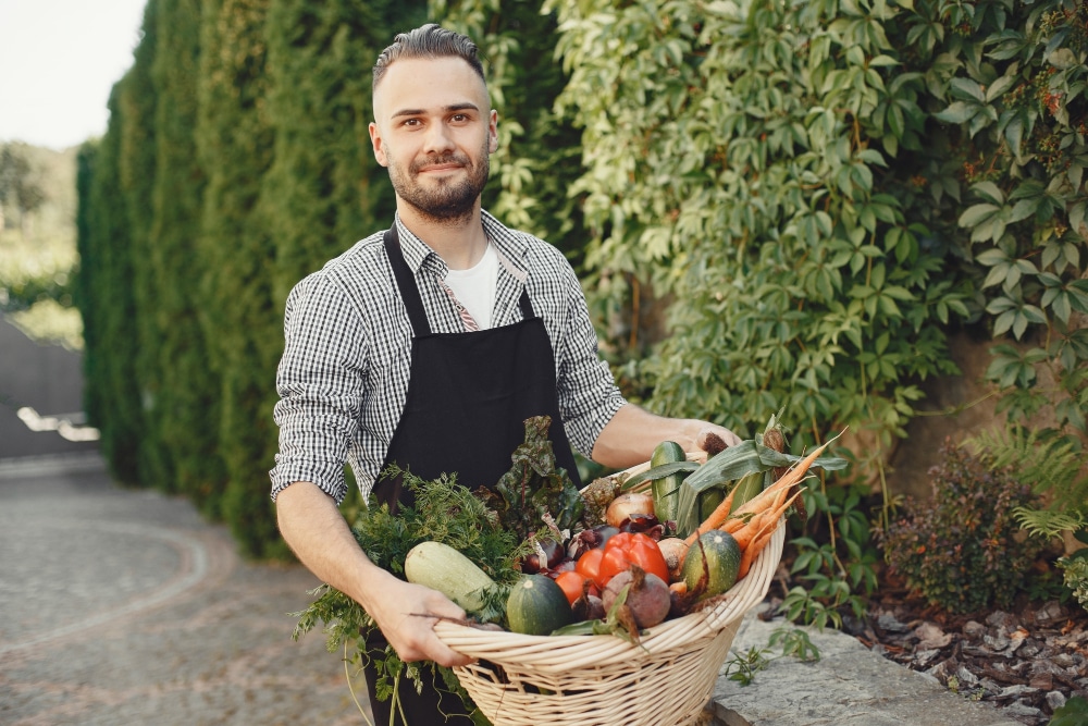 man holding a vegetable basket near a garden protected with agricultural netitng